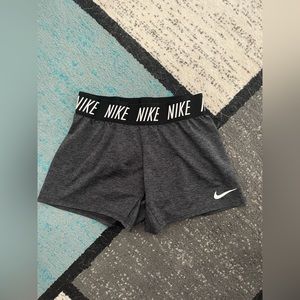 Dark grey women’s Nike shorts with a black band with white “Nike” lettering.